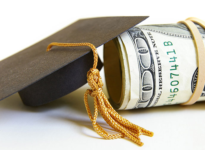 Rolled up dollar bills under a small black graduation cap.