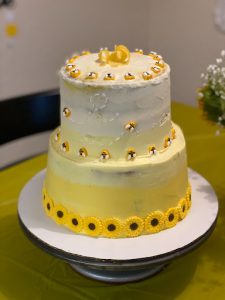 A multi-tiered cake with flowers and yellow and white frosting made by Alexis.