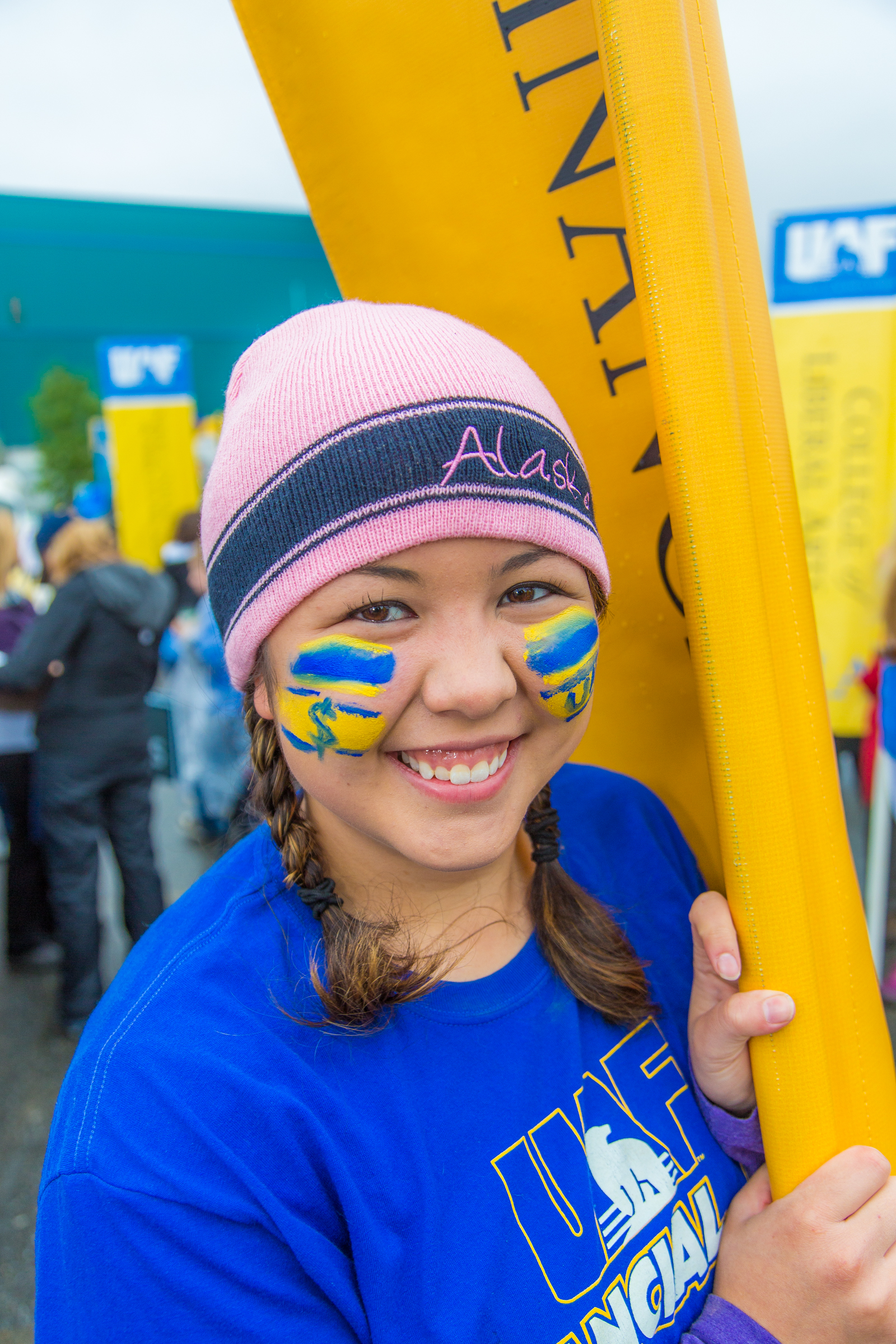 A person wearing a pink Alaska hat and wearing a blue UAF shirt. Their face is painted in blue and yellow.